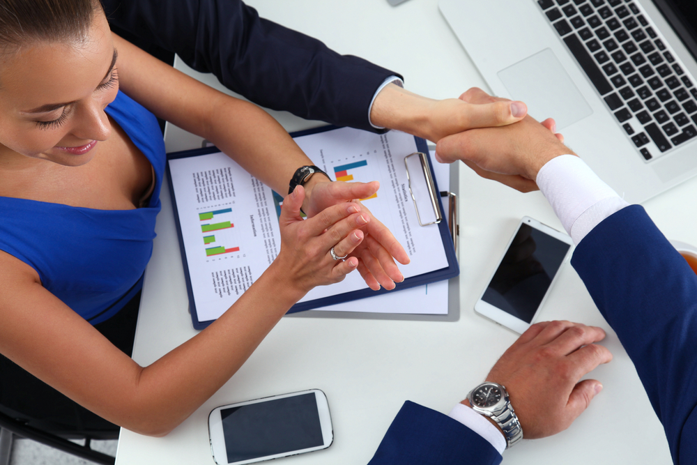 Businessmen in a handshake agreement in a meeting with a woman clapping